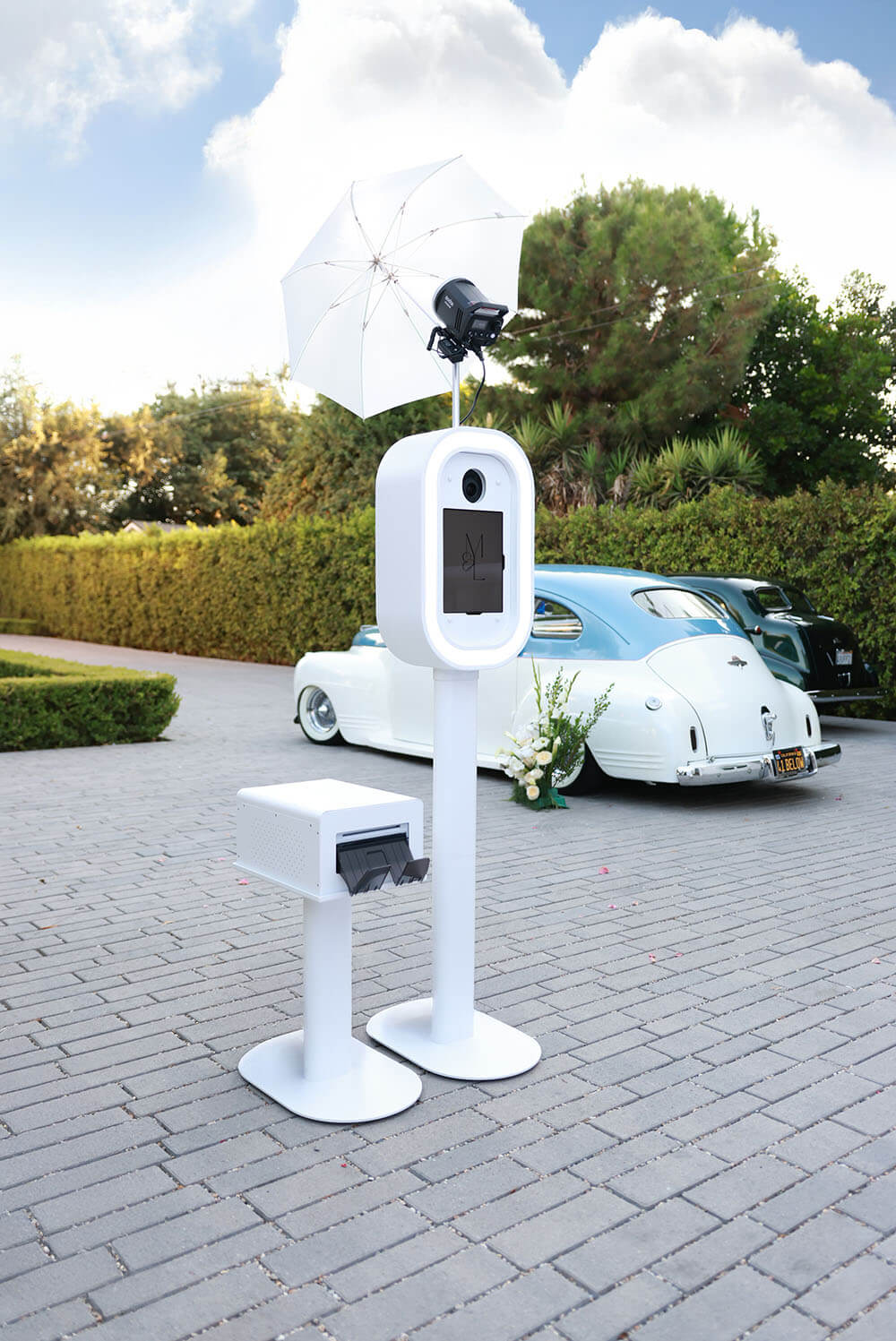 a photobooth outside with print station and a vintage car in the background